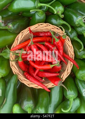 Peperoni caldi in un cestino circondato da peperoni verdi caldi. Foto Stock