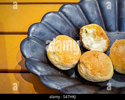 Vista ad alto angolo di mini pompini di crema alla vaniglia in ciotola nera su un tavolo di legno giallo. Foto Stock