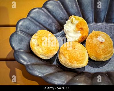 Vista ad alto angolo di mini pompini di crema alla vaniglia in ciotola nera su un tavolo di legno giallo. Foto Stock