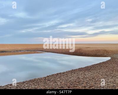 Nuvole che si riflettono sulla laguna a Shingle Street nel Suffolk, Inghilterra, Regno Unito. Foto Stock