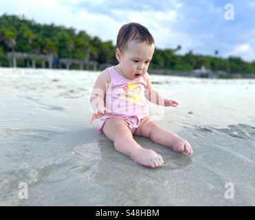 Bambino con un'espressione di fascino sul viso quando entra un'onda e l'acqua raggiunge i piedi Foto Stock