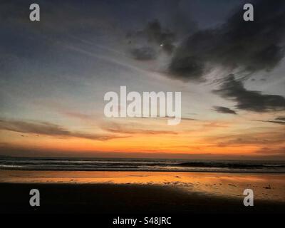 Tramonto sulla spiaggia di Seminyak Bali con il sole tramontare sul mare e il bagliore arancione che rimane nelle nuvole Foto Stock