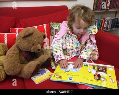 Toddler che legge un libro nella biblioteca Foto Stock