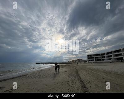 Ampio paesaggio di una spiaggia vuota con il sole che tramonta dietro le nuvole a Palavas con due bambini, il fratello maggiore e la sorellina, Occitanie, vicino a Montpellier, in Francia Foto Stock