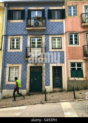 Lisbona, Portogallo - 13 settembre 2024: Edificio tradizionale portoghese con piastrelle azulejo blu, balconi e persiane verdi su un lastricato in pendenza Foto Stock