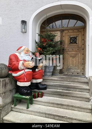 La figura di Babbo Natale è seduta su una scala di fronte a una vecchia porta d'ingresso in legno Foto Stock