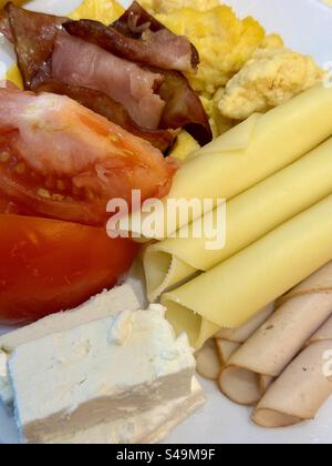 Piatto da colazione con uova strapazzate, pancetta, prosciutto, formaggio a fette, pomodori freschi, formaggio feta e tacchino deli. Foto Stock