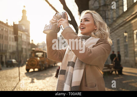 Giovane bella Allegra donna bionda di scattare le foto con il suo film vintage fotocamera su una giornata di sole in piazza Rynok di Lviv, Ucraina Foto Stock