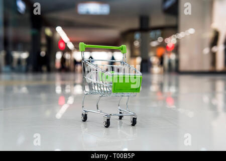 Poco carrello della spesa su un pavimento piastrellato di vuoto al centro dello shopping. Concetto di comprare le cose in Mall. Toy carrello al supermercato di sfocatura dello sfondo. Pu Foto Stock