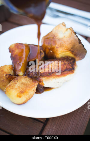 Pollo arrosto cena con Yorkshire pudding. Il sugo di carne che viene versato sopra la parte superiore Foto Stock