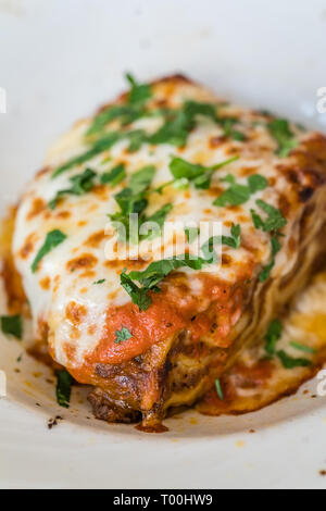 Porzione di una deliziosa lasagna di carne di manzo con formaggio cheddar di fusione, mozzarella e ricotta formaggi, guarnite con prezzemolo Foto Stock