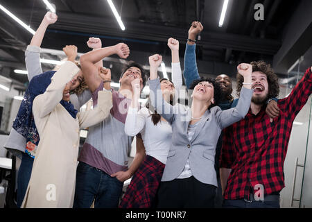 Ritratto di giovane eccitato multiethnics business team di sviluppatori di software in piedi e guardando la fotocamera mentre si celebra il successo all'avvio moderno Foto Stock