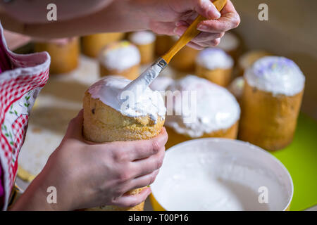 Un baker spazzole di un liquido mantecato glassa di zucchero sulla parte superiore di una tradizionale torta di Pasqua realizzata da pasticceria e cotto in forme cilindriche per decorare il t Foto Stock