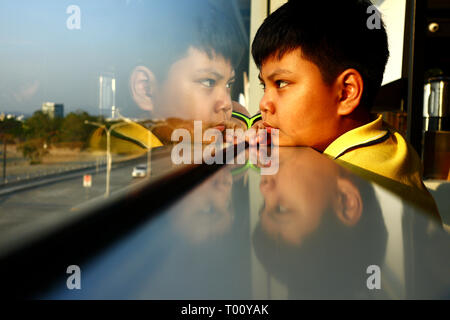 Foto di un giovane ragazzo asiatico guardando fuori una finestra di vetro Foto Stock