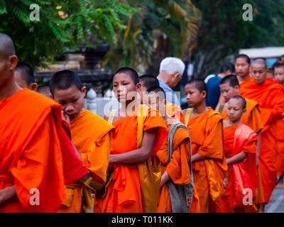 I monaci buddisti in arancione vesti coda per mattina alms dando cerimonia, Luang Prabang, Laos Foto Stock