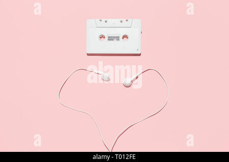 Bianco di cassette audio e forma di cuore delle cuffie su un sfondo rosa. L'amore degli anni novanta il concetto di partito. Foto Stock