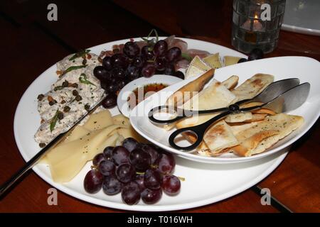 Piatto ripieno di antipasti assortiti tra cui formaggio, uva, pane e molto altro. Foto Stock