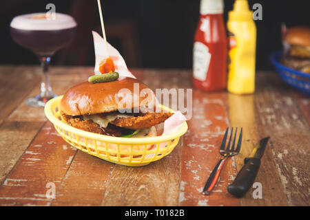 Hamburger di pollo in un cestello con un cocktail su una tavola di legno con ketchup e senape Foto Stock