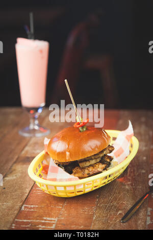 Hamburger di pollo servito in un cestello con un frullato su un tavolo di legno Foto Stock