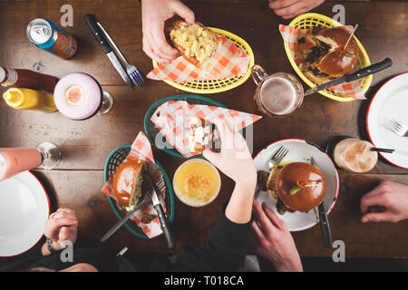 Gli amici condividono il cibo da bar hot dog, hamburger e cocktail Foto Stock