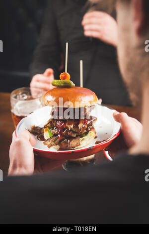 Un cameriere serve una grassa hamburger di manzo su una piastra di metallo in un ristorante Foto Stock