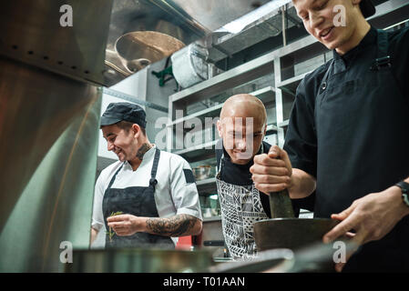 Sto guardando la rigorosa chef in grembiule guardando attentamente come il suo lavoro di assistente presso il ristorante la cucina. Concetto di cucina a vista. Foto Stock