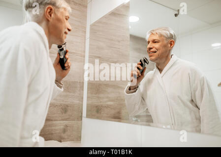 Allegro uomo adulto rade in corrispondenza dello specchio nella stanza da bagno Foto Stock