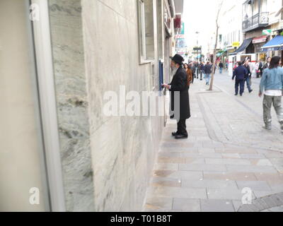 Scena di strada ebraica di uomo in piedi di fronte di ATM su una strada in Gibilterra Foto Stock