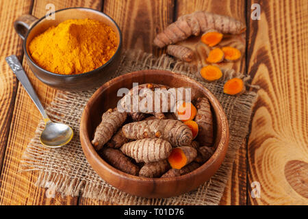 Curcuma radici e polvere in ciotole sul vecchio tavolo in legno Foto Stock