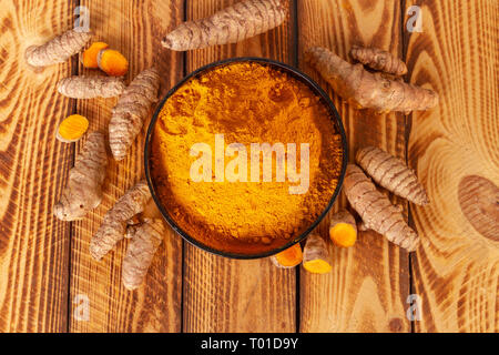 Sovraccarico di curcuma in polvere e la curcuma radici su sfondo di legno Foto Stock