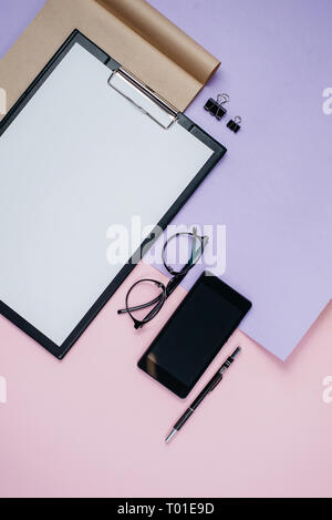 Piatti creativi di laici che, vista dall'alto ufficio scrivania. Area di lavoro con vuoto clip board, forniture per ufficio, penna, notepad, smartphone, occhiali in rosa e v141 Foto Stock