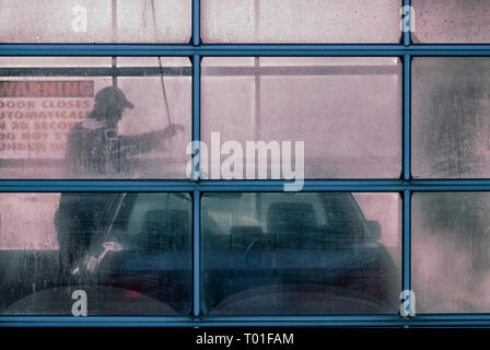 L'uomo il suo lavaggio auto utilizzando una rondella a pressione in corrispondenza di un self service carwash Foto Stock