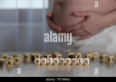 Parola ECLAMPSIA composto da lettere di legno. Donna incinta in background Foto Stock