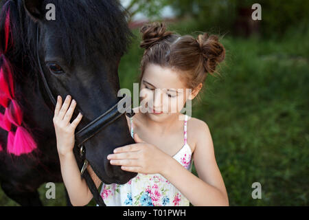 Carino bambina con pony nero nel parco. Chiudi immagine Foto Stock