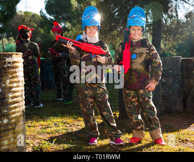 Due amici, un ragazzo e una ragazza in camuffamento in posa con pistole su outdoor paintball campo da gioco Foto Stock