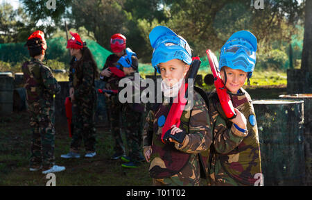 Due amici, un ragazzo e una ragazza in camuffamento in posa con pistole di marcatore su outdoor paintball campo da gioco Foto Stock