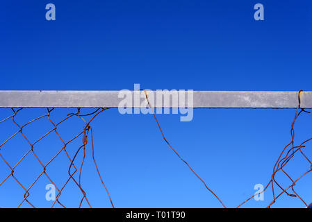 Rotto e danneggiato opaco filo di maglia recinto con un cielo blu e un intero nella scherma Foto Stock