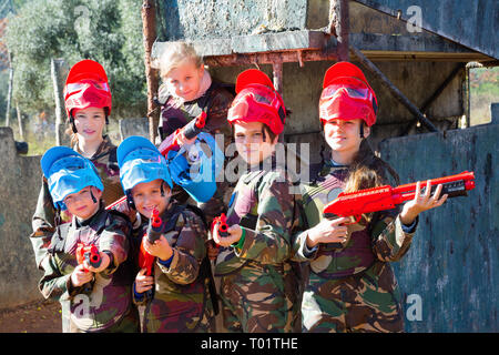 Gentile lieto allegro gruppo di bambini paintball giocatori in camuffamento in posa con pistole di paintball sul campo da gioco all'aperto Foto Stock