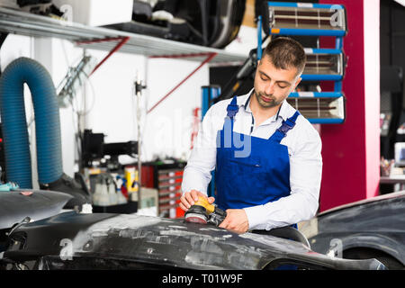 Professional repairman in auto officina sabbiatura paraurti di automobili, la preparazione per la verniciatura Foto Stock