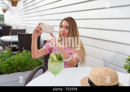 Bella ragazza nelle mani di uno smartphone, le chiamate per una chiamata video nelle cuffie. Applicazione online reti sociali online, fotografie. Una donna in Foto Stock