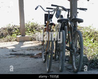 Tre biciclette appoggiata contro un palo di legno in una struttura all'aperto Foto Stock