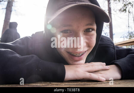 Un giovane adolescente di sesso maschile nella soleggiata all'aperto in mostra il suo ortodonzia o rinforzi su i suoi denti Foto Stock