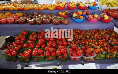 Un assortimento di rosso, arancione e giallo pomodori venduti in scaffali in un aperto il mercato all'aperto Foto Stock