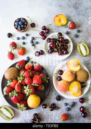 Varie di bacche e frutti su sfondo grigio. Fragole, ciliegie, kiwi, pesche, i mirtilli. Vista dall'alto. Spazio di copia Foto Stock