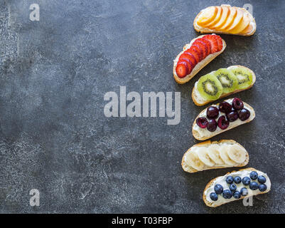 Varie di bacche e frutti su un piatto di legno su sfondo grigio. Fragole, ciliegie, kiwi, pesche, mirtilli su una piastra. Vista superiore Foto Stock