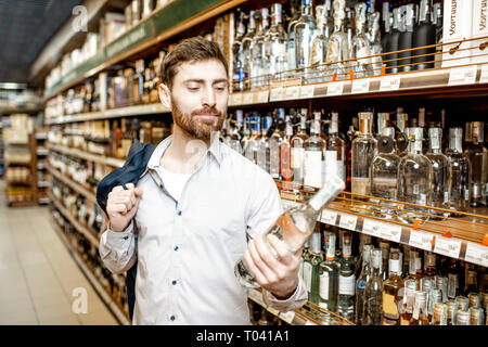 Ritratto di un uomo con una sete di alcool, in piedi vicino a ripiani con bevande forti nel supermercato Foto Stock