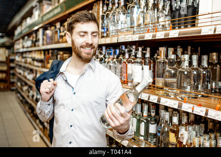 Ritratto di un uomo con una sete di alcool, in piedi vicino a ripiani con bevande forti nel supermercato Foto Stock