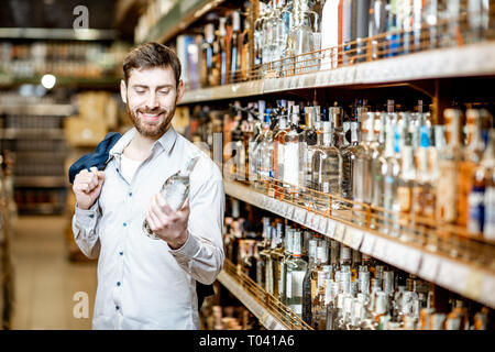 Ritratto di un uomo con una sete di alcool, in piedi vicino a ripiani con bevande forti nel supermercato Foto Stock