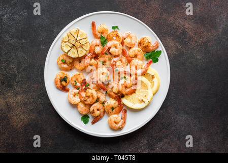 Gamberi arrosto con limone, aglio ed erbe aromatiche. Frutti di mare, shelfish. Gamberi in padella con spezie, aglio e limone su sfondo nero, copia dello spazio. Foto Stock