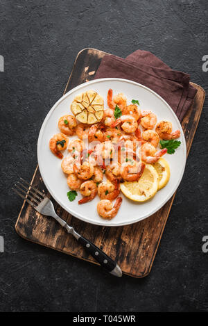 Gamberi arrosto con limone, aglio ed erbe aromatiche. Frutti di mare, shelfish. Gamberi in padella con spezie, aglio e limone su pietra nera di sfondo, copia Foto Stock